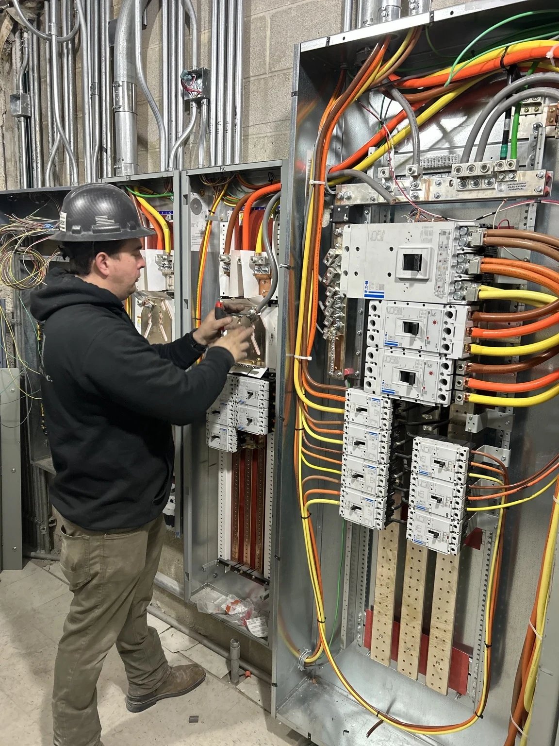 Electrician installing connections at electrical distribution equipment during the Altitude Roscoe Village buildout.
