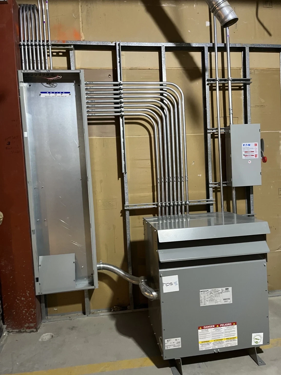 Transformer, disconnect and conduit routing beside a wall-mounted panel enclosure.