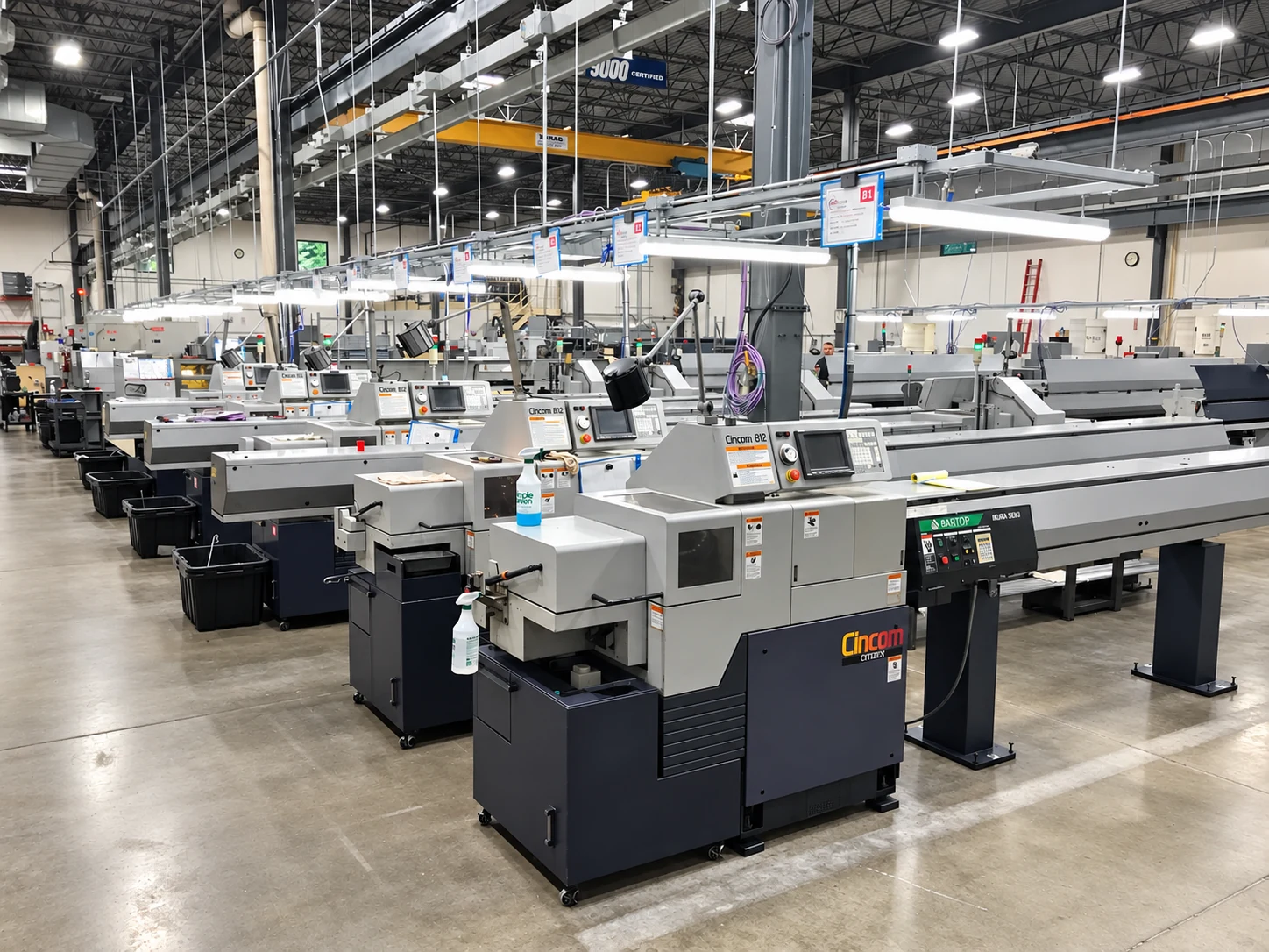Rows of CNC lathes with overhead rack-mounted lighting and a bridge crane in the background.