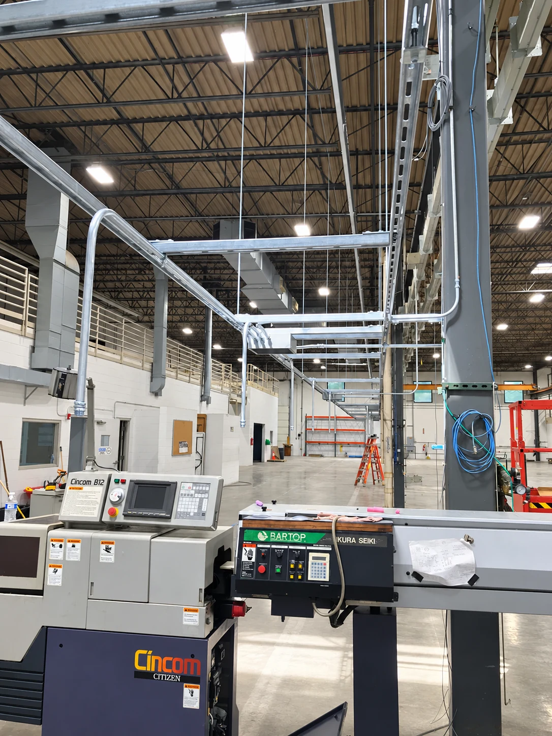 Unistrut support rack and conduit above a CNC machine and bar feeder.