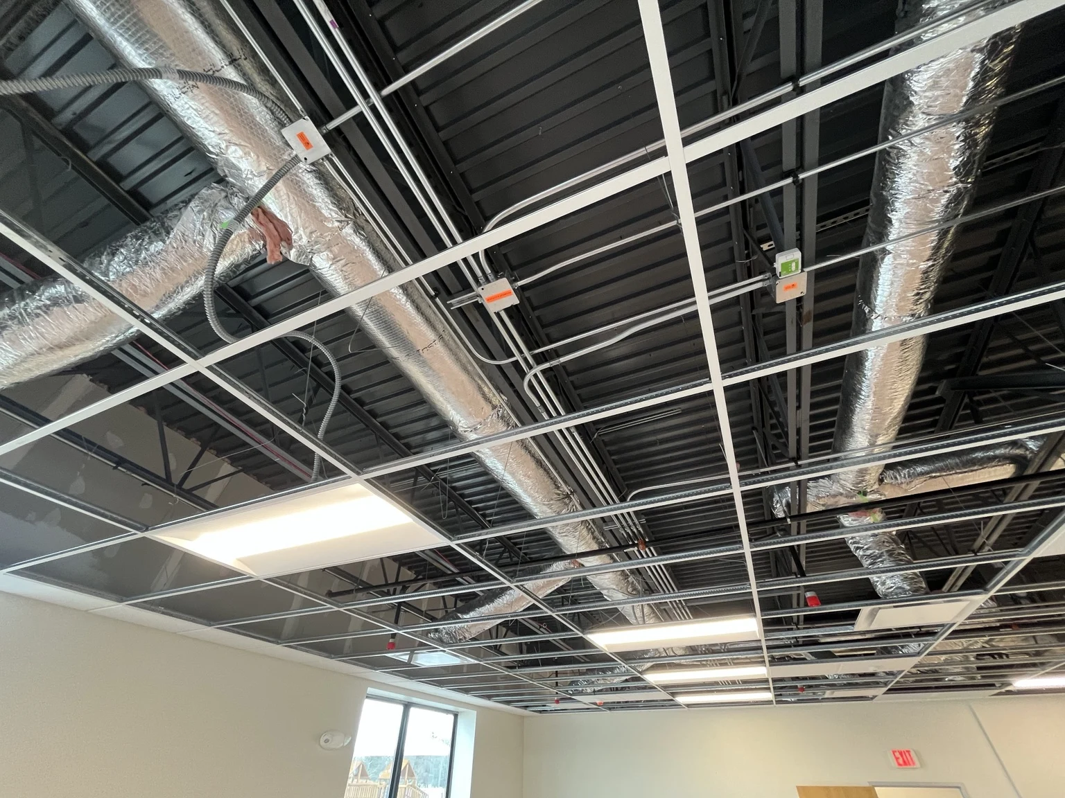 Overhead electrical conduit, junction boxes and lighting above the classroom ceiling grid during construction.