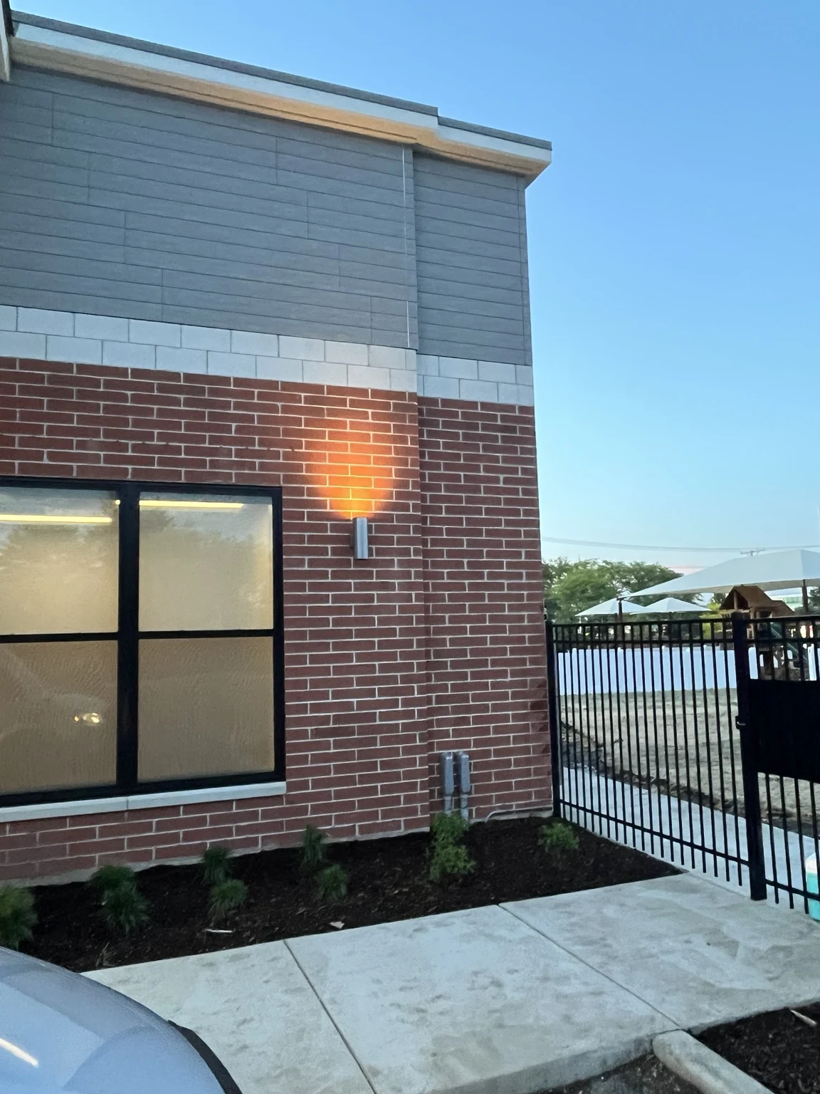 Exterior architectural wall sconce beside a classroom window and fenced outdoor area.