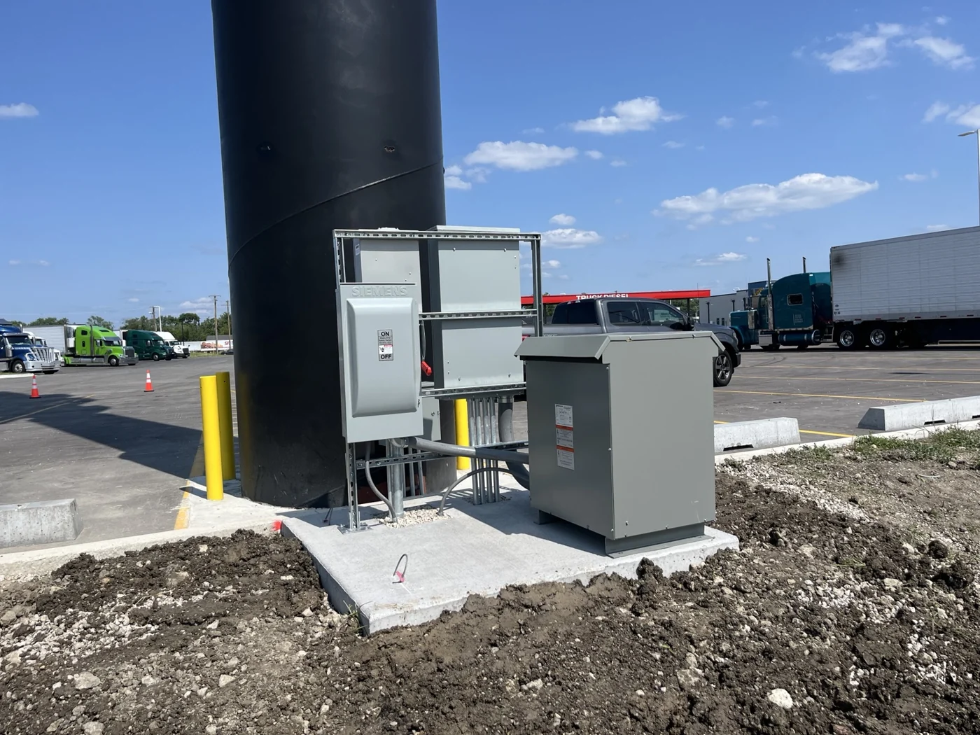 Transformer, disconnect, and equipment supports installed on a precast concrete pad beside the Ricky Rockets high-rise sign.