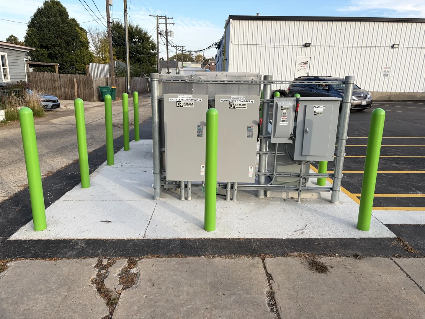 Outdoor disconnects and distribution panel on a galvanized support rack surrounded by green bollards.