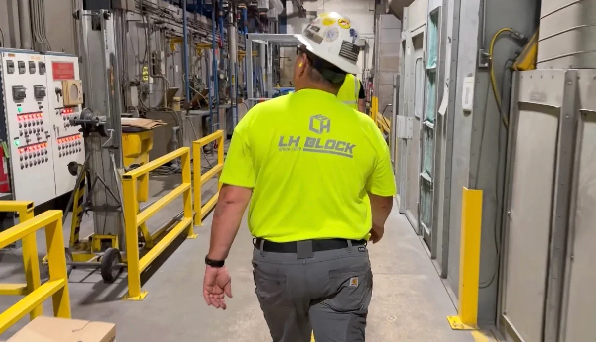 LH Block employee in a high-visibility shirt and hard hat reviewing a manufacturing area beside electrical equipment.