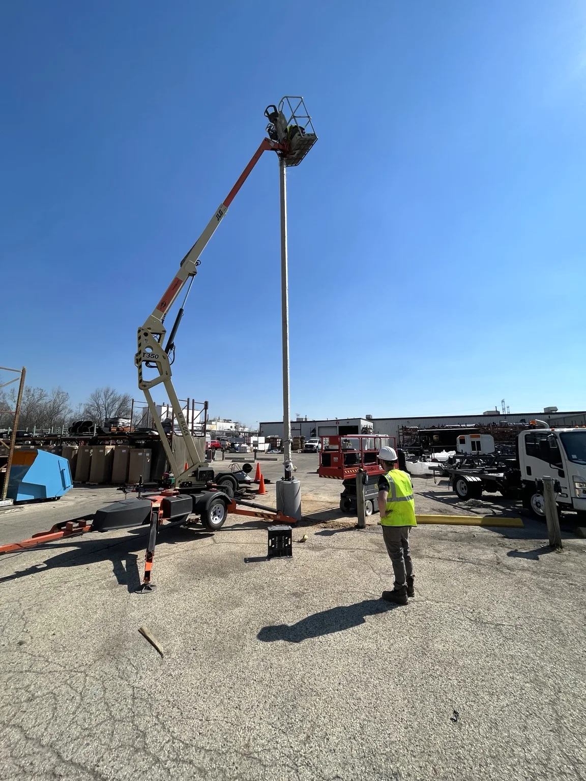 Crew and boom truck positioning a tall light pole in the outdoor storage area.