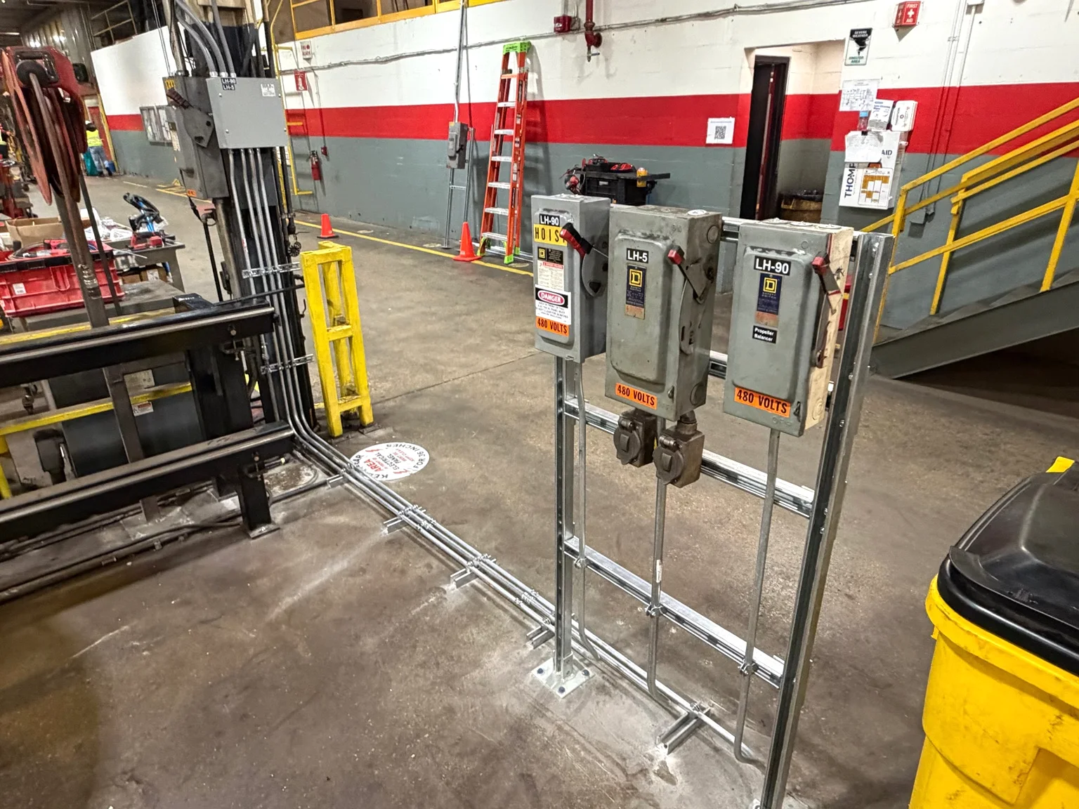 Equipment disconnects and conduit on support racks beside a manufacturing aisle.