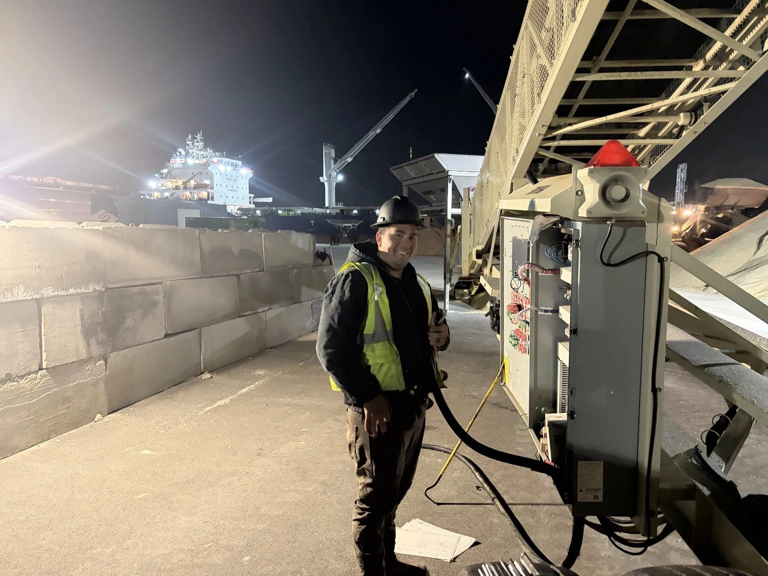 Electrician beside the conveyor at Midwest Salt’s Chicago yard, with a vessel in the background.