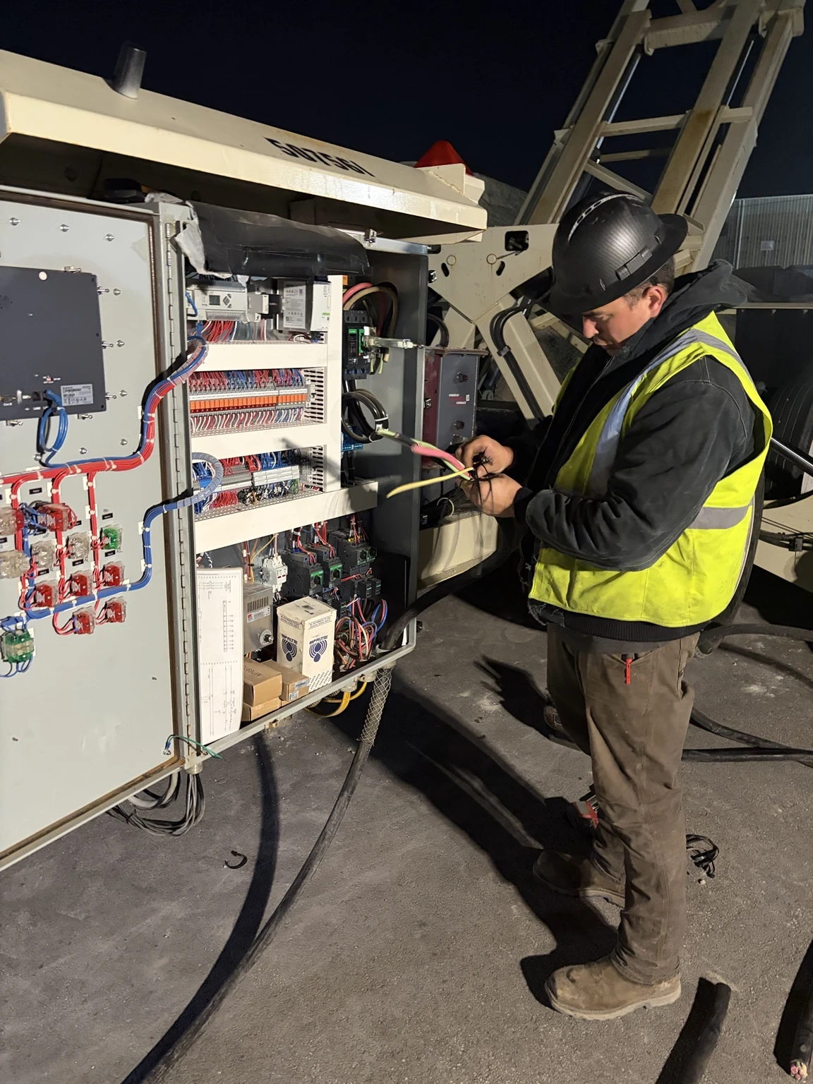 Electrician working on the conveyor supply cable beside the open electrical enclosure.