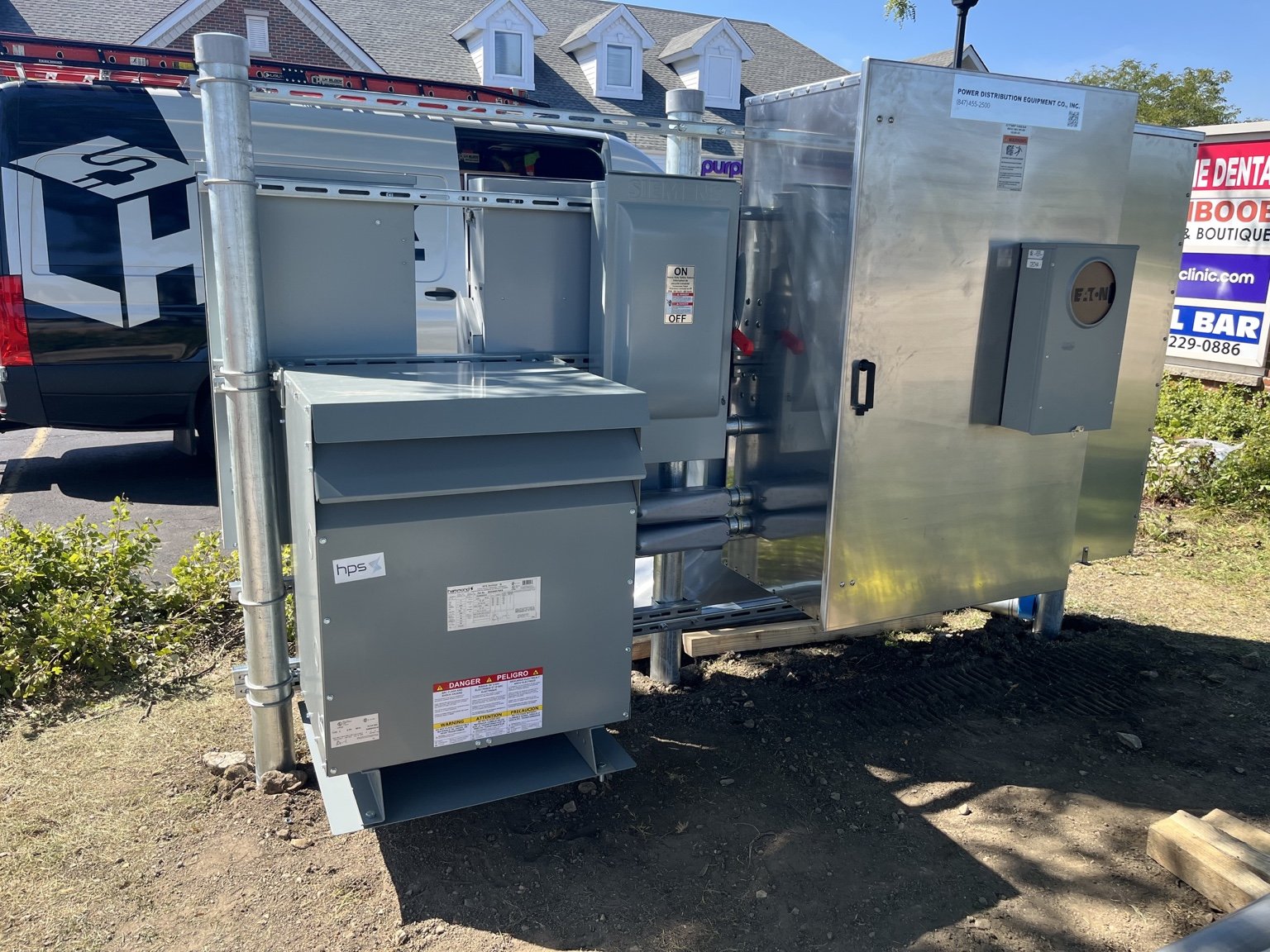 Outdoor electrical service equipment beside an LH Block service van in Naperville.