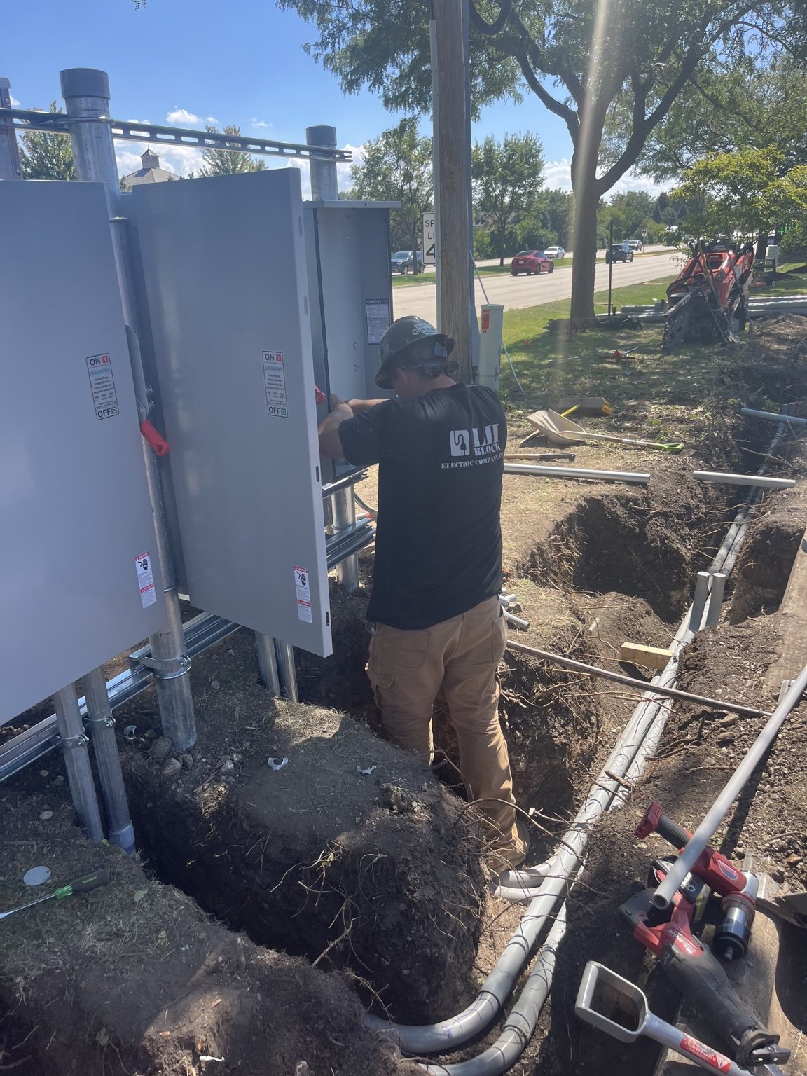 Worker beside an underground conduit trench at the Naperville EV charging project.