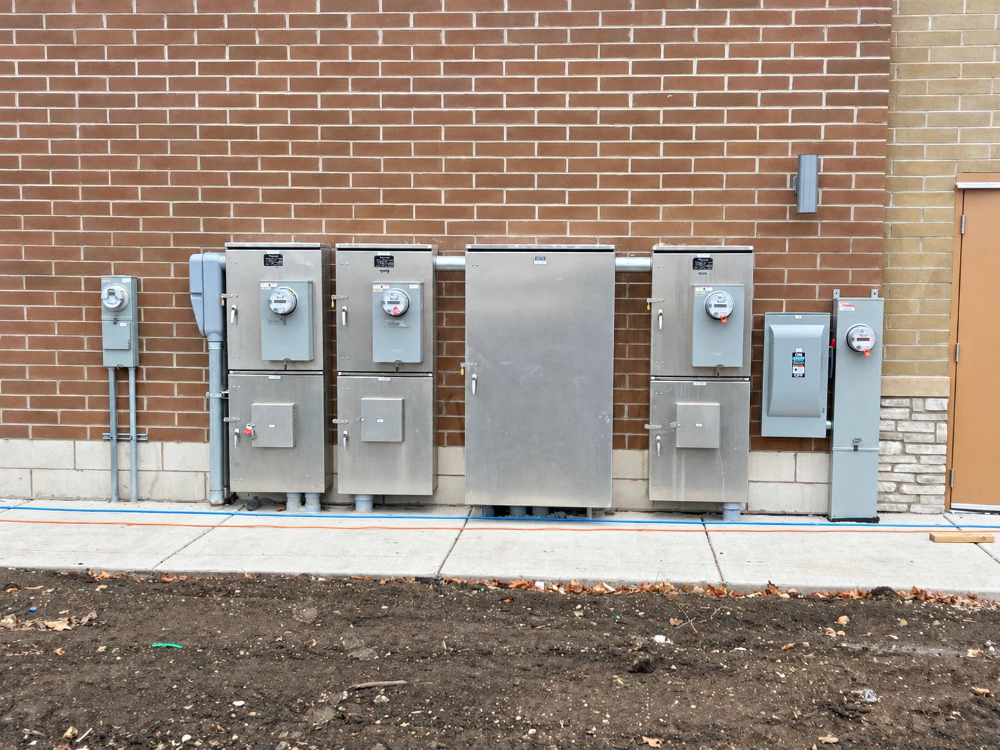 Exterior tenant meters, disconnect cabinets, and distribution equipment mounted on a brick building.