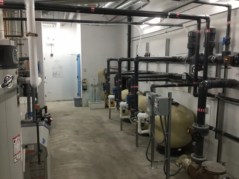 Pool filtration tanks, piping, electrical controls, and equipment connections in a mechanical room