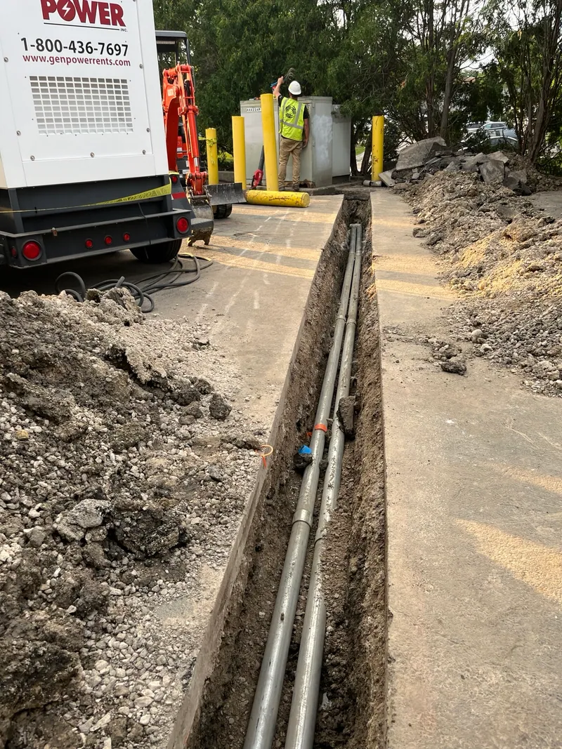 Parallel underground conduits in the saw-cut trench leading toward the transformer.
