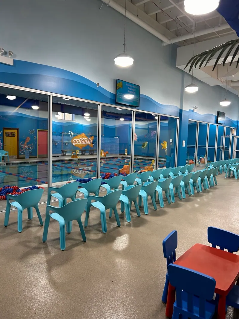 Suspended lighting above turquoise seating beside windows overlooking a Goldfish Swim School pool