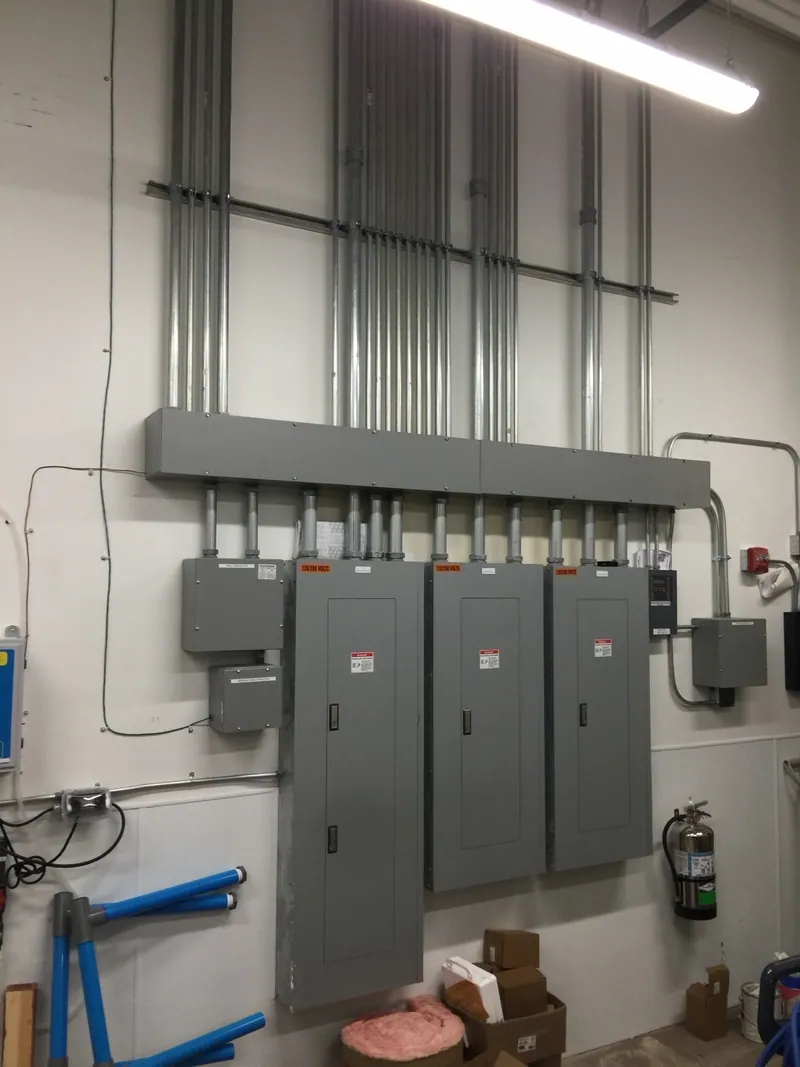 Three electrical panelboards beneath a wireway and vertical conduit runs